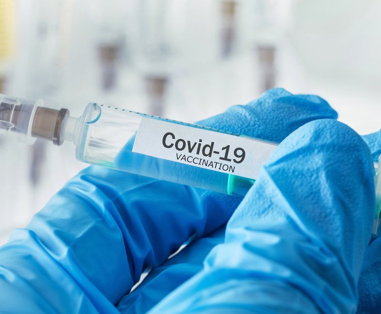 COVID-19 vaccination shot, held between fingers in medical gloves