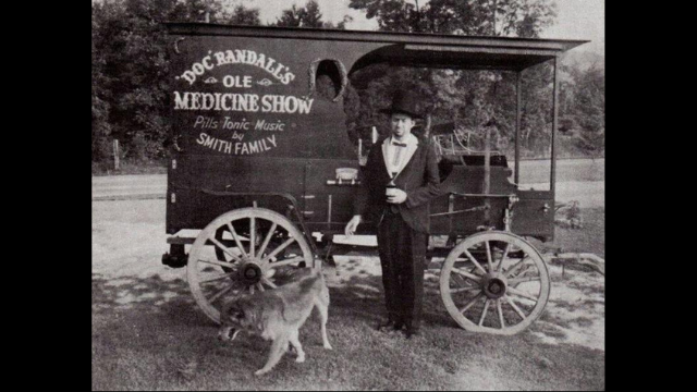 Black and white photo of Doc Randall's Ole Medicine Show wagon, with man in a top hat and a dog.