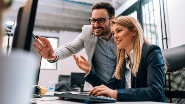 Two professionals looking at a screen talking and smiling in an office environment