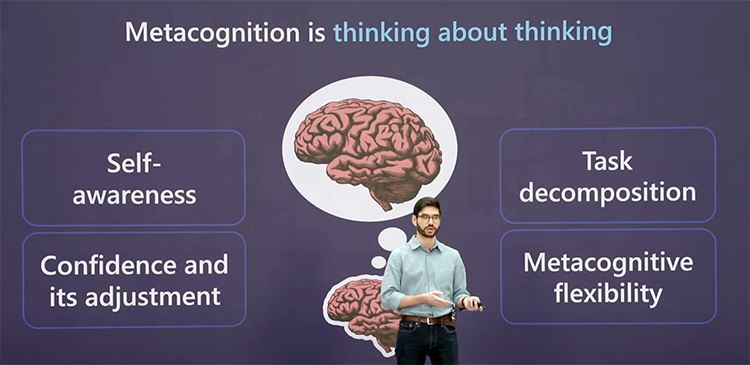 A man in a green button-up and jeans stands in front of a purple background, giving a presentation. Behind him are some graphics of human brains and thought bubbles alongside the text "Self-awareness," "Task decomposition," "Metacognitive flexibility," and "Confidence and its adjustment."