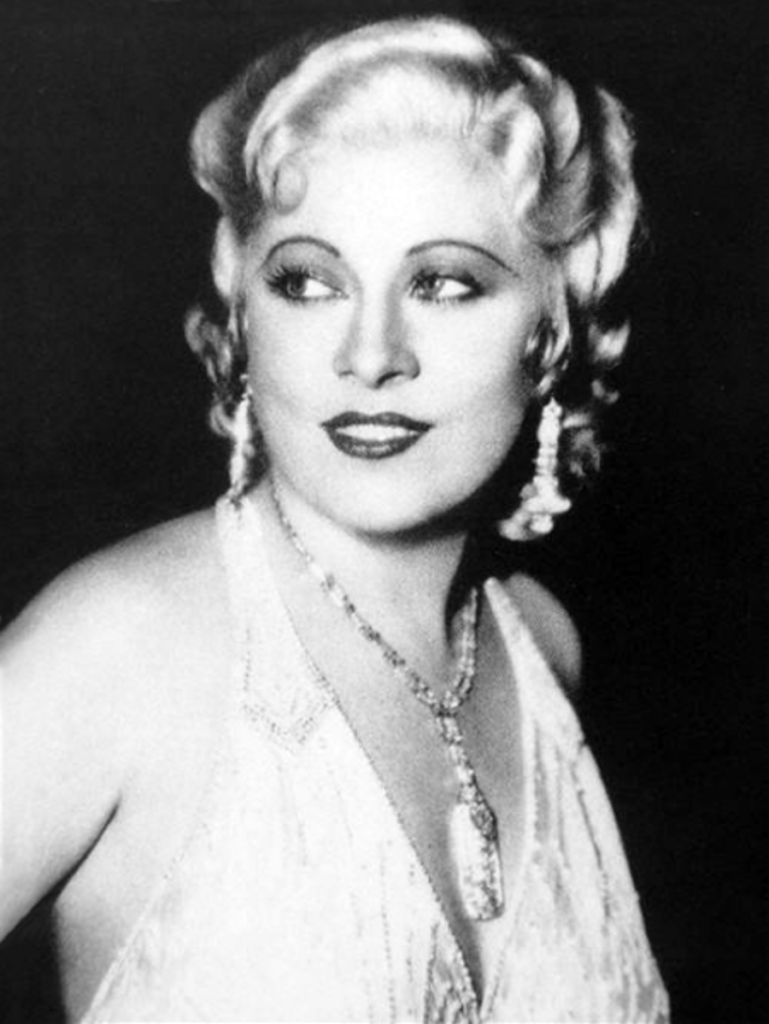 Mae West, dressed up and bejeweled.