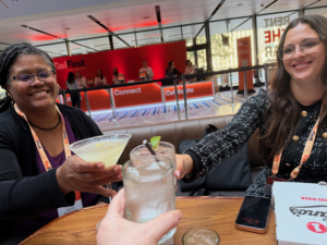 Three RelFest attendees sitting around a table, toasting drinks and smiling.